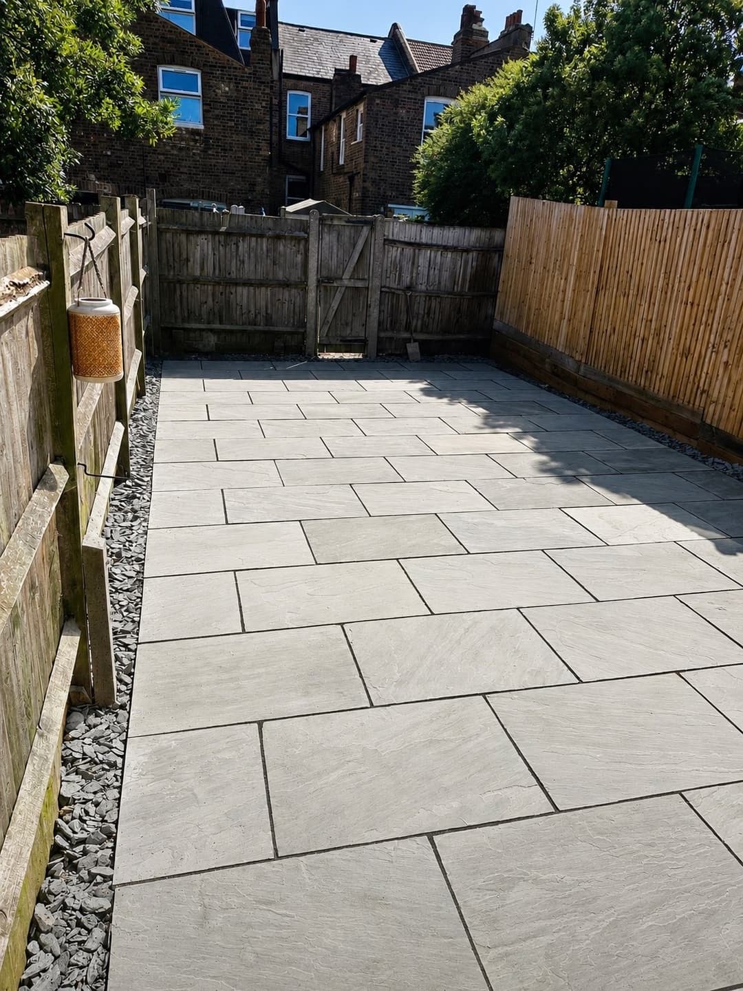 A completed garden rebuild with a Kandla grey sandstone patio laid in a random pattern, slate gravel borders and new closeboard fencing