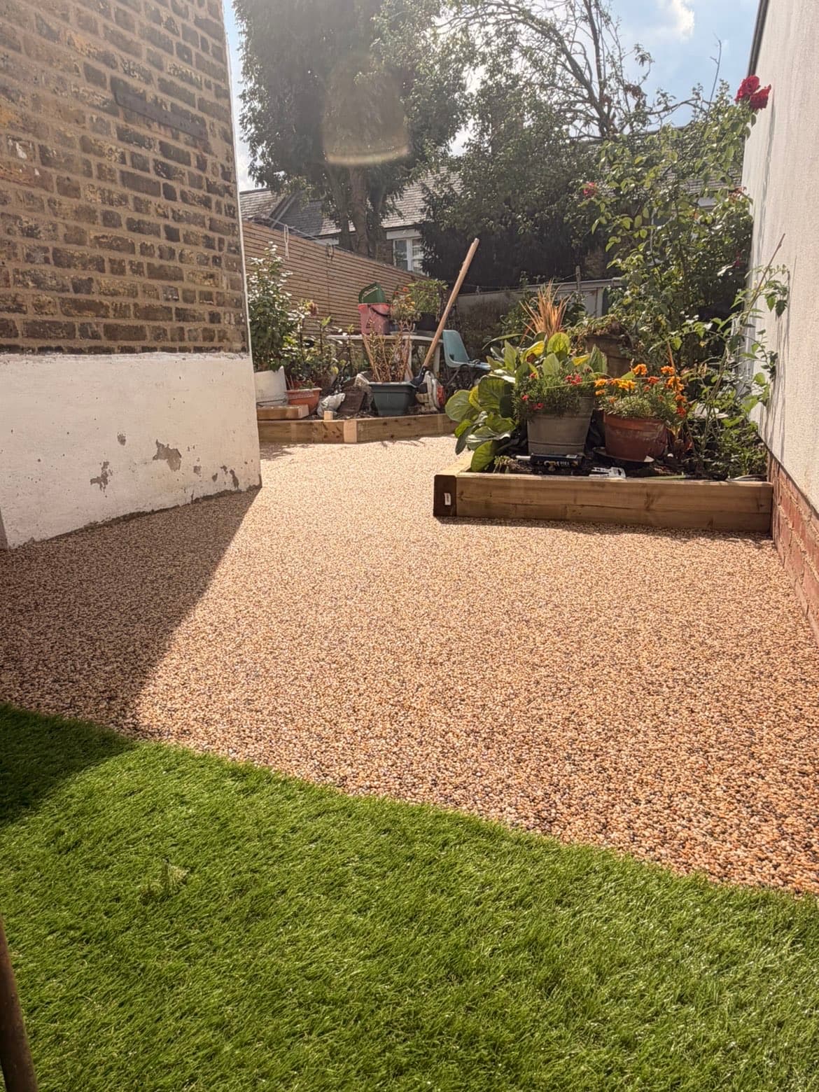 Resin bound gravel area meeting a newly laid artificial grass lawn with timber sleeper raised beds to one side