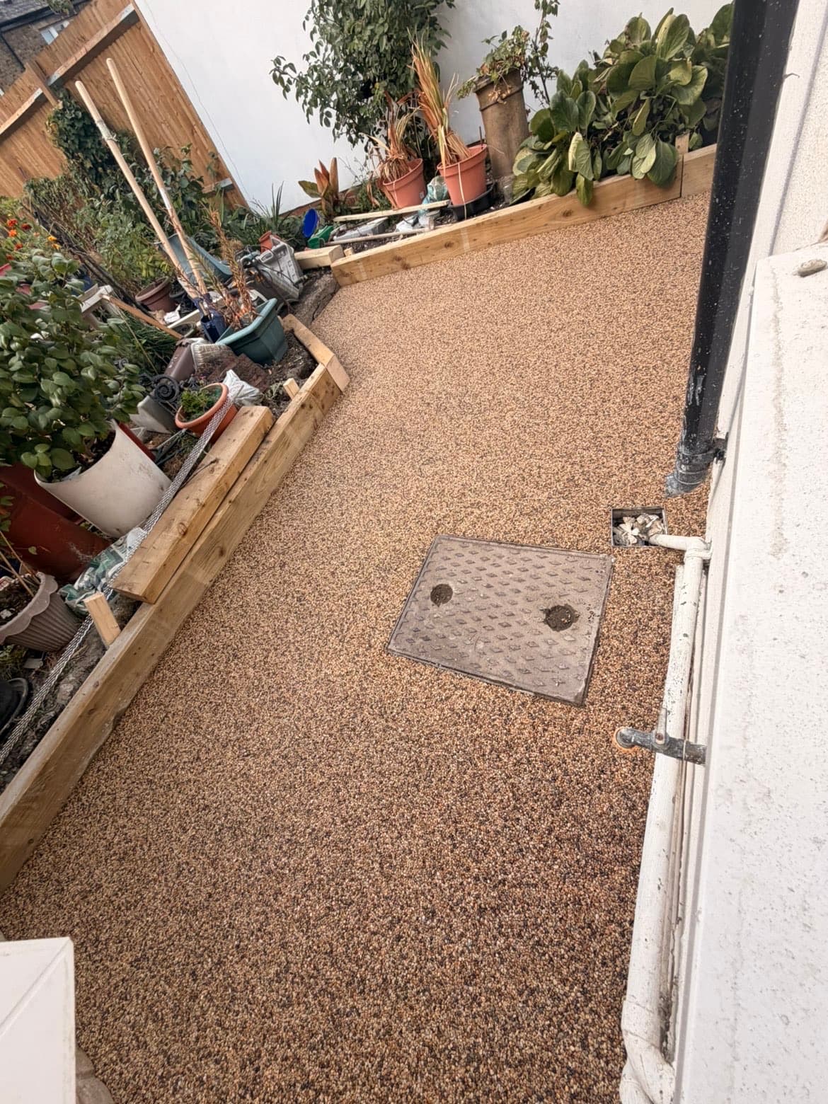 Resin bound path curving around the side of the house with a drain inspection cover set flush into the surface