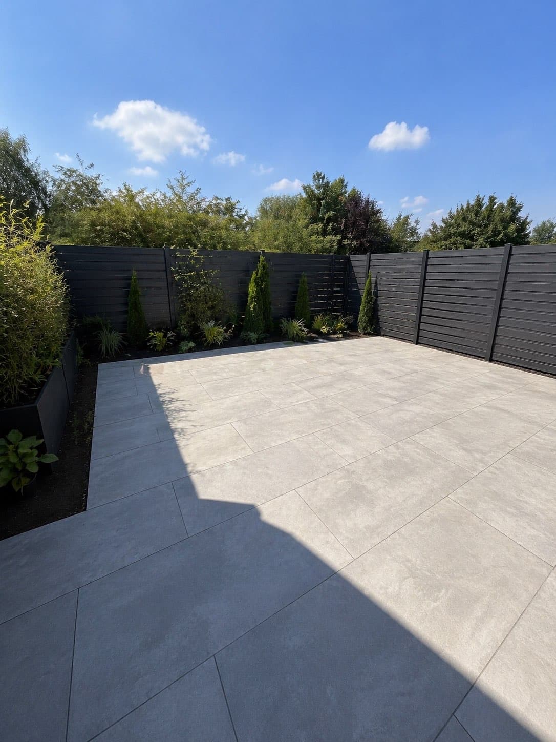 Large grey porcelain patio with dark composite fencing and planted border