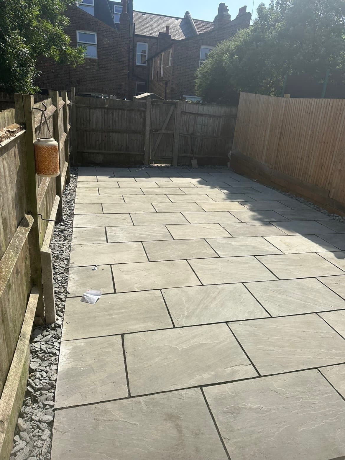 Kandla grey sandstone patio with riven texture and slate chipping borders along timber fencing