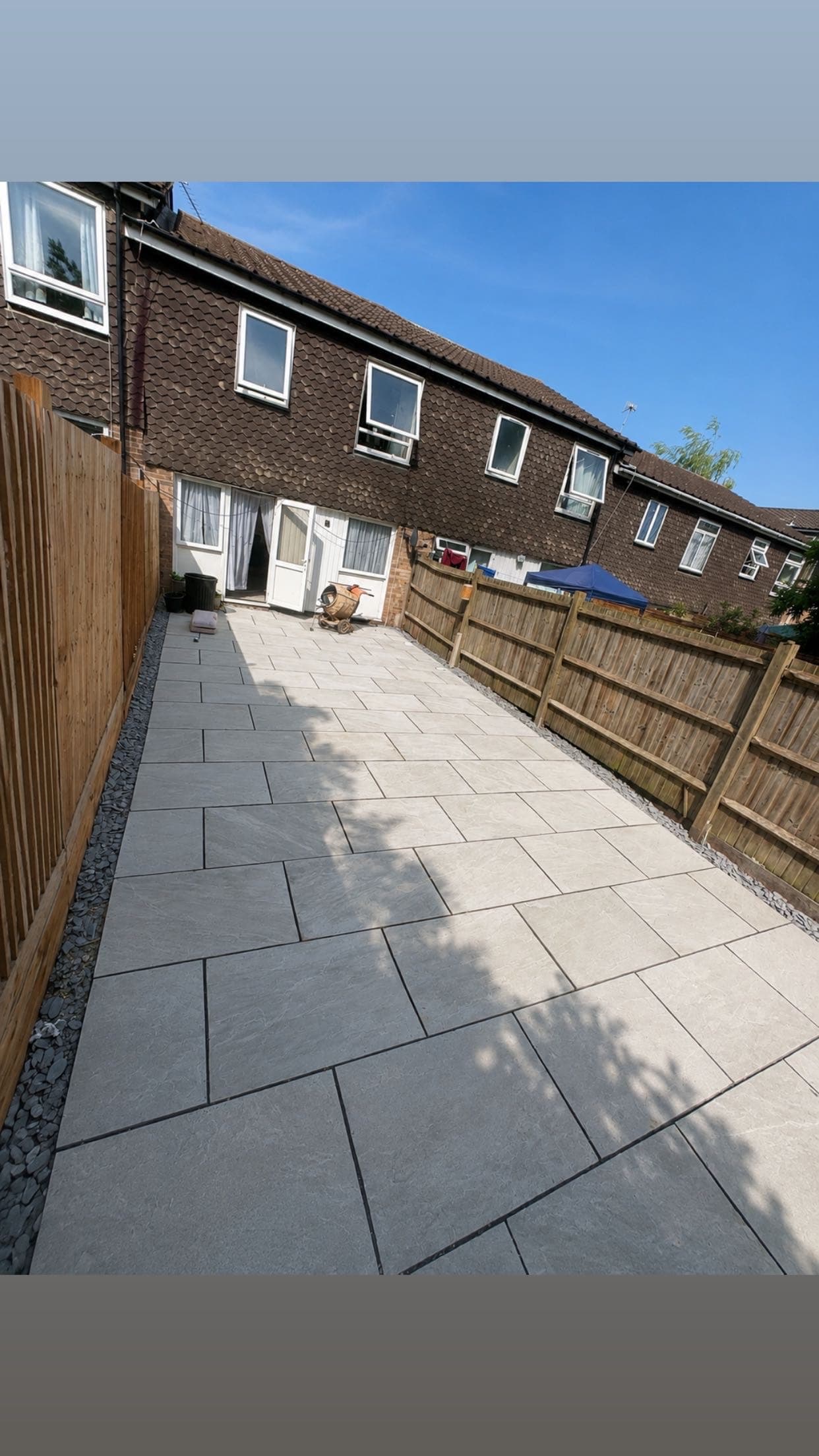 Finished Kandla grey sandstone patio running the full length of a back garden with slate borders