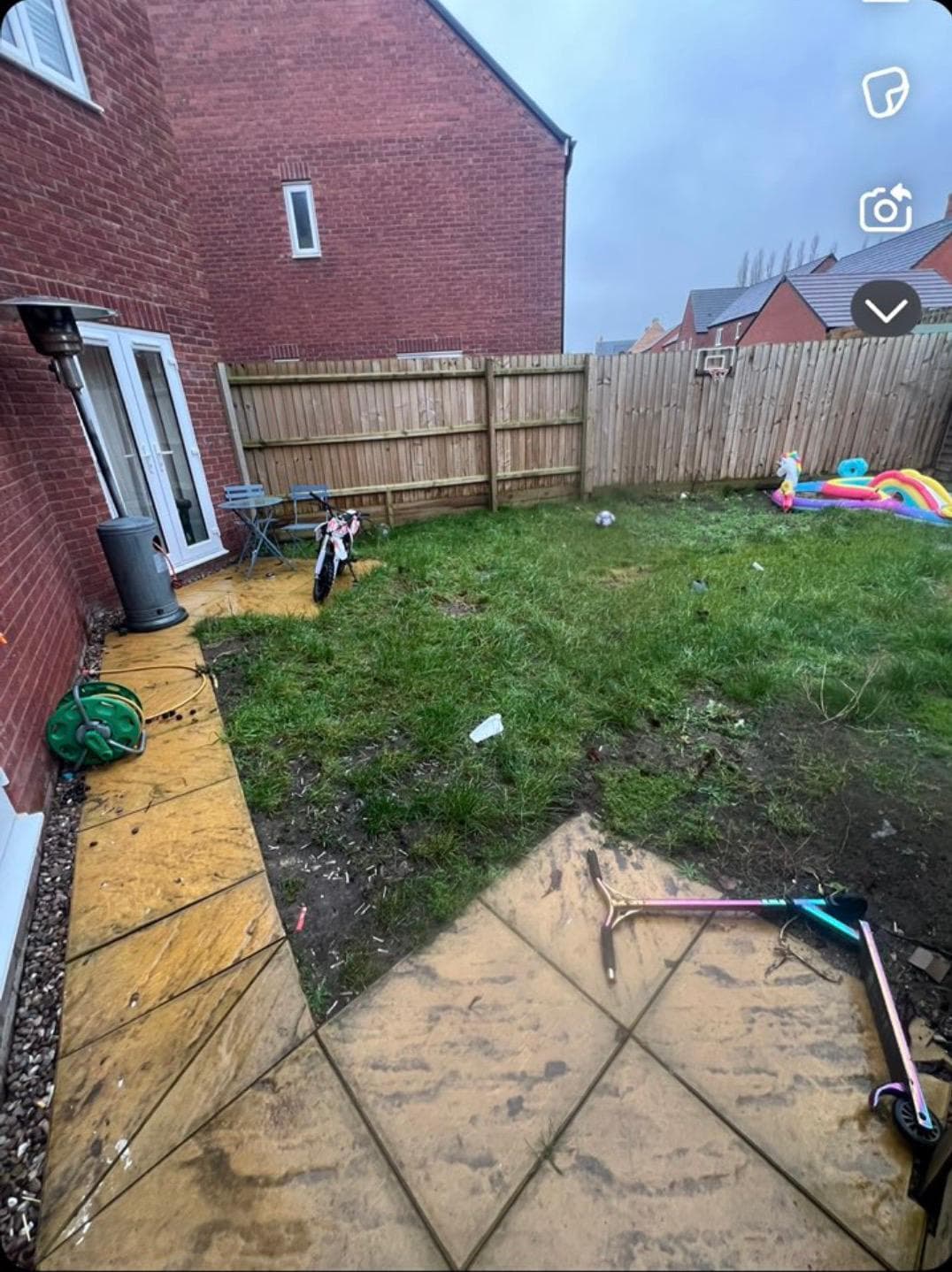 Before photo showing worn yellow paving and patchy lawn with wooden fence